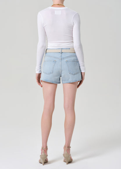 Person wearing light blue denim shorts and a white long-sleeve top on a plain background