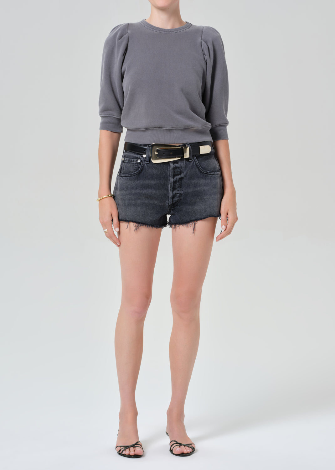 Person wearing a gray sweater and denim shorts on a plain background