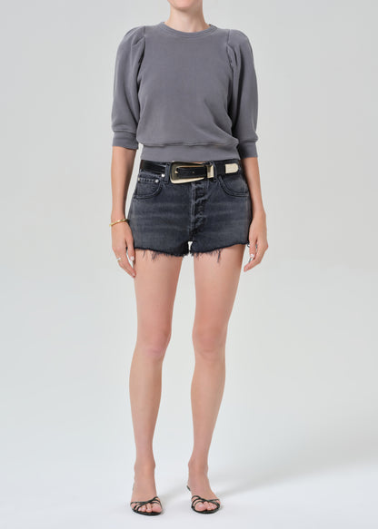 Person wearing a gray sweater and denim shorts on a plain background