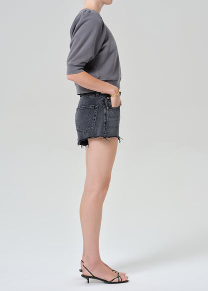 Person wearing a gray sweatshirt and black denim shorts on a grey background