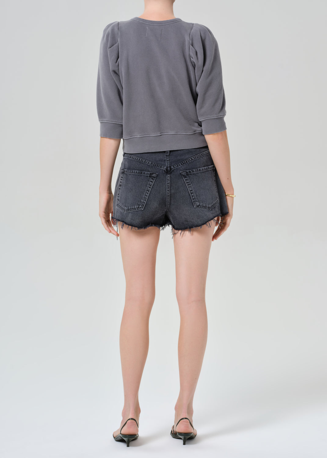 Person wearing a gray sweatshirt and black denim shorts on a grey background