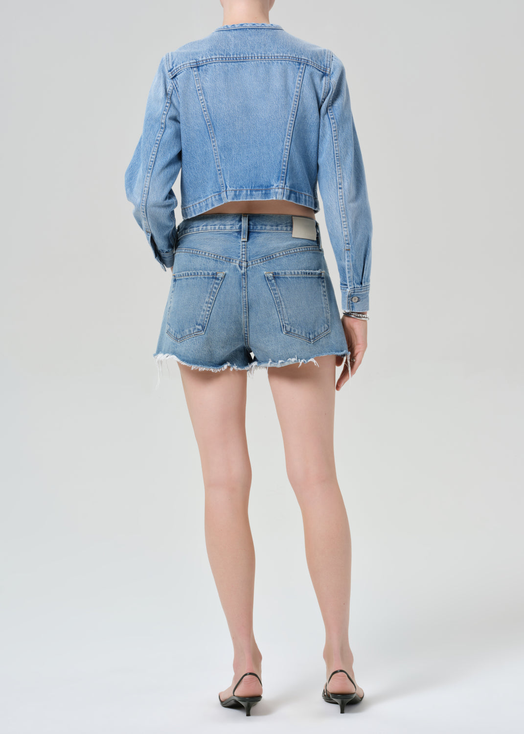 Person wearing a denim jacket and shorts on a plain background