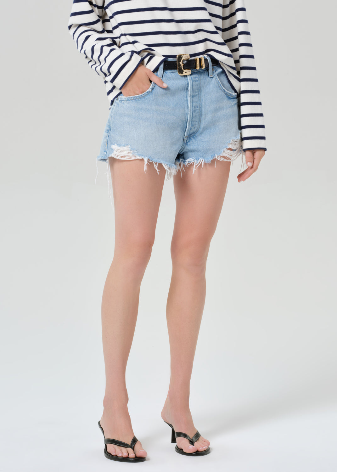 Person wearing a striped long-sleeve shirt and denim shorts on a grey background