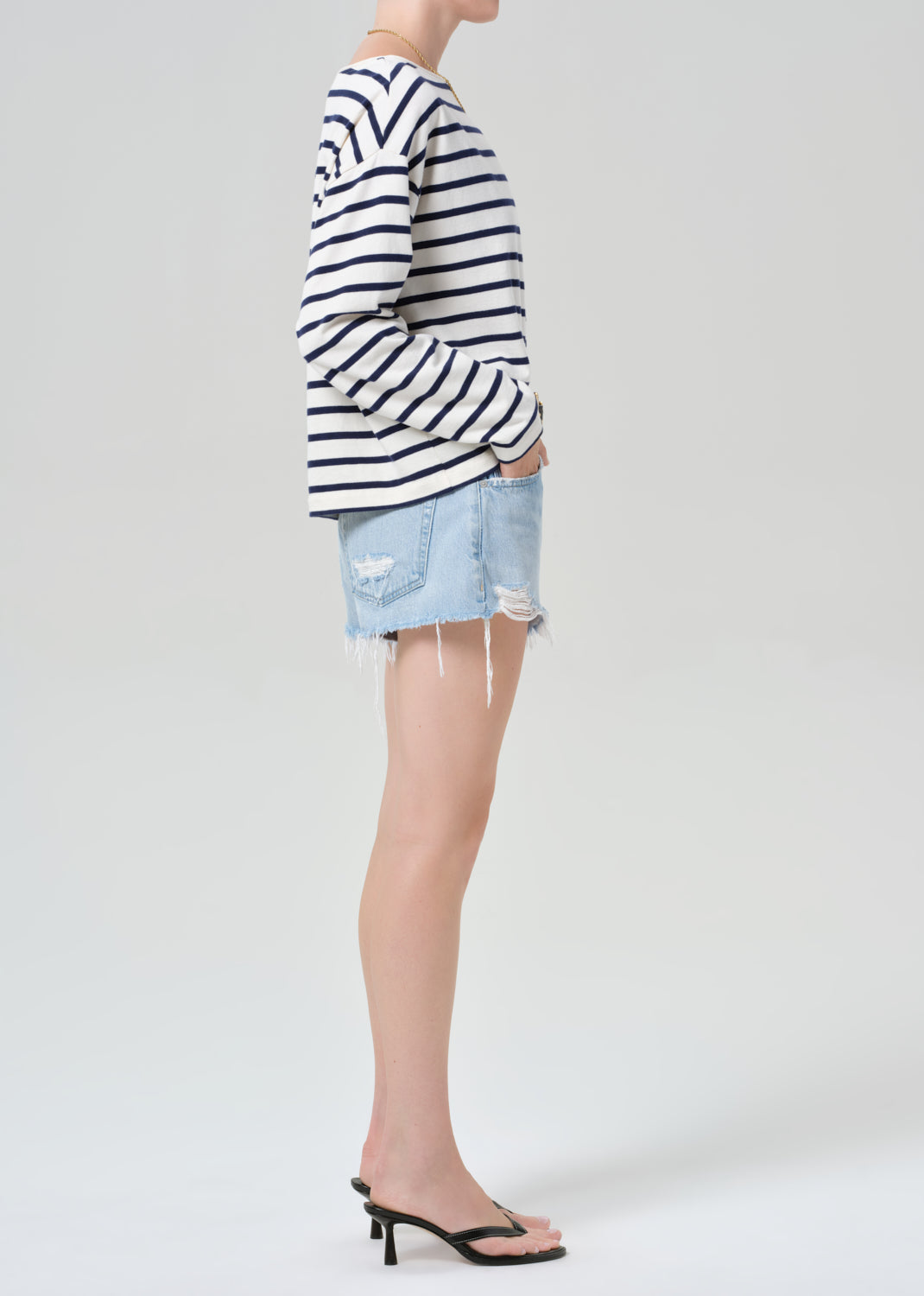 Person wearing a striped long-sleeve shirt and denim shorts on a grey background