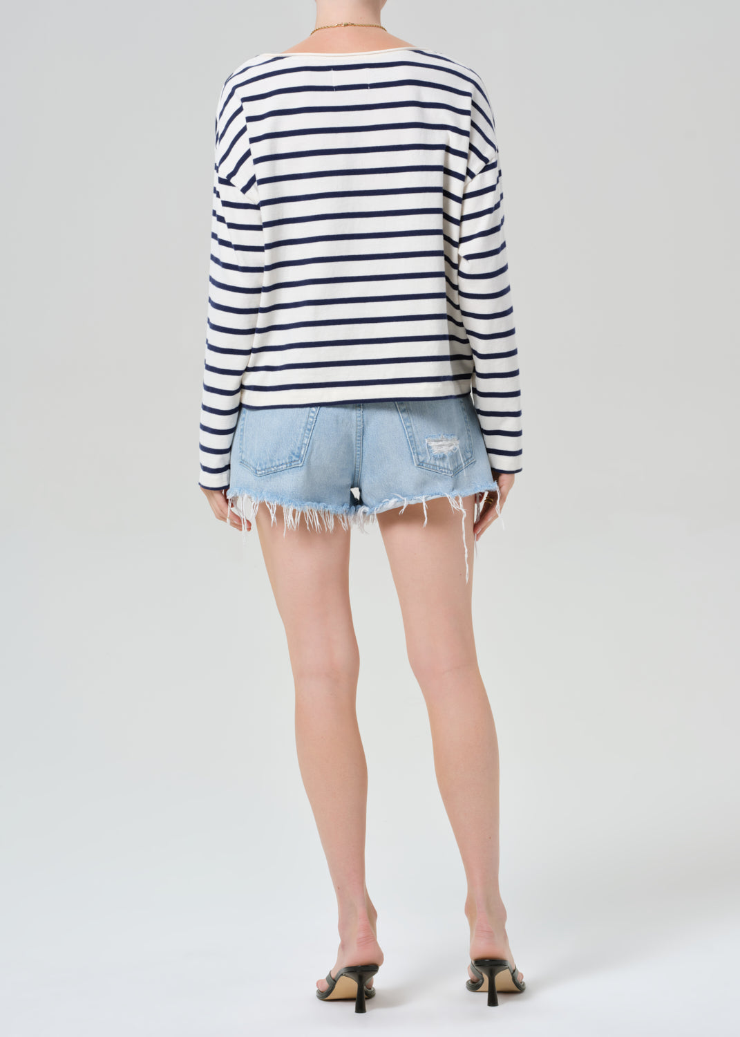 Person wearing a striped long-sleeve shirt and denim shorts on a grey background