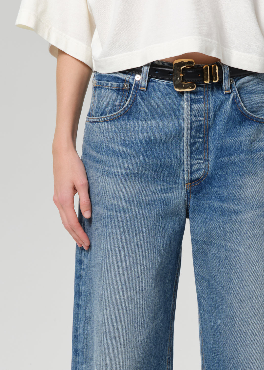 Person wearing blue jeans with a white shirt on a plain background