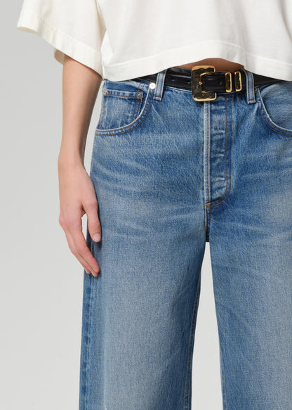 Person wearing blue jeans with a white shirt on a plain background
