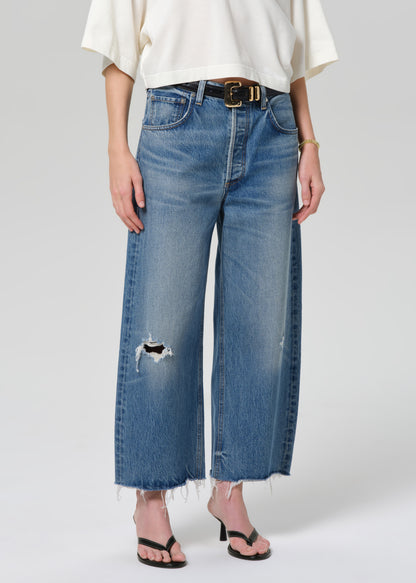Person wearing blue jeans with a white top on a plain background