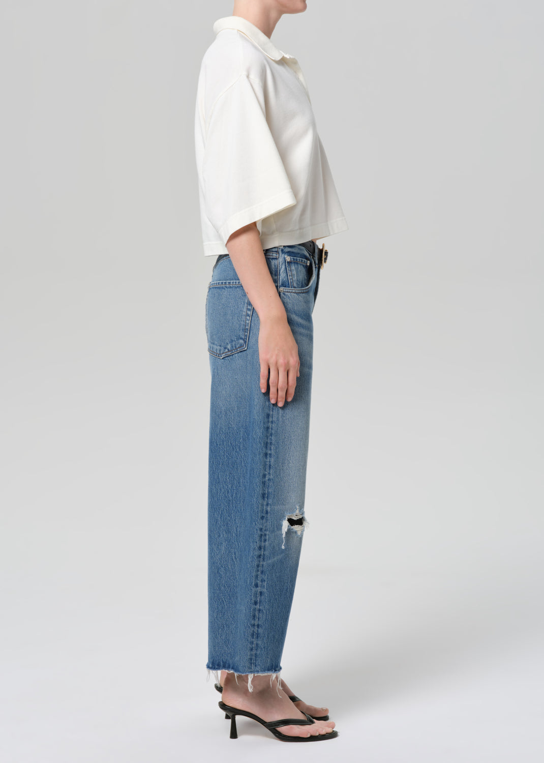 Person wearing a white shirt and blue jeans on a plain background