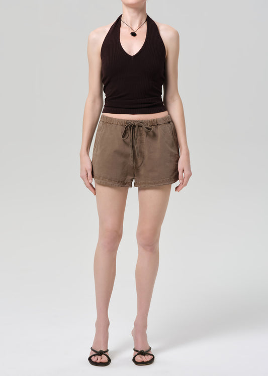 Person wearing a black halter top and brown shorts on a gray background