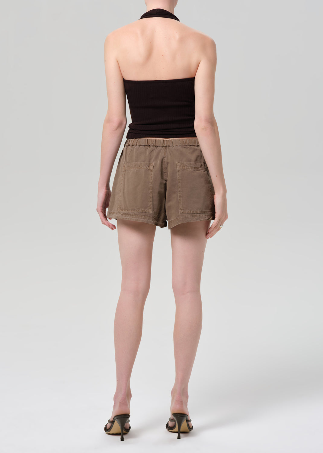 Person wearing a black halter top and brown shorts on a plain background
