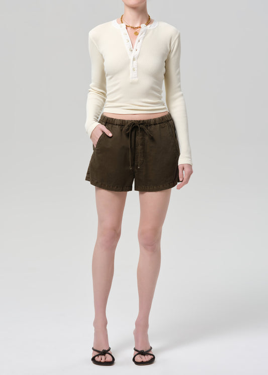 Person wearing a cream long-sleeve shirt and brown shorts on a plain background