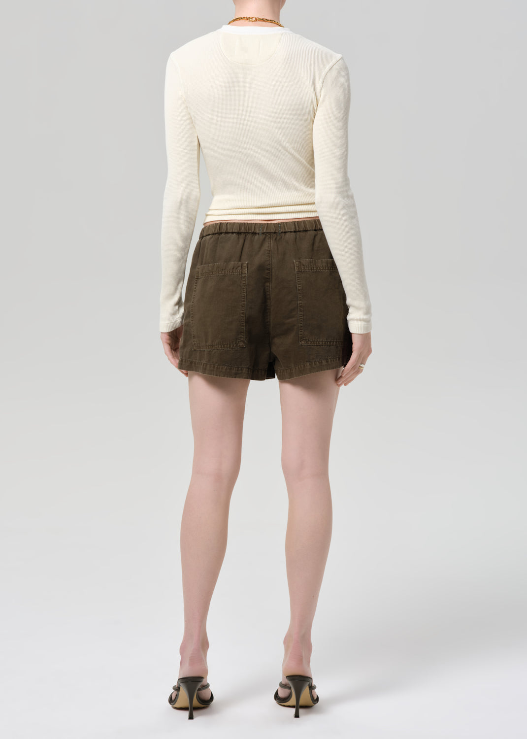 Person wearing a cream long-sleeve shirt and brown shorts on a plain background