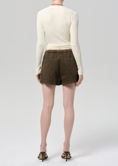 Person wearing a cream long-sleeve shirt and brown shorts on a plain background