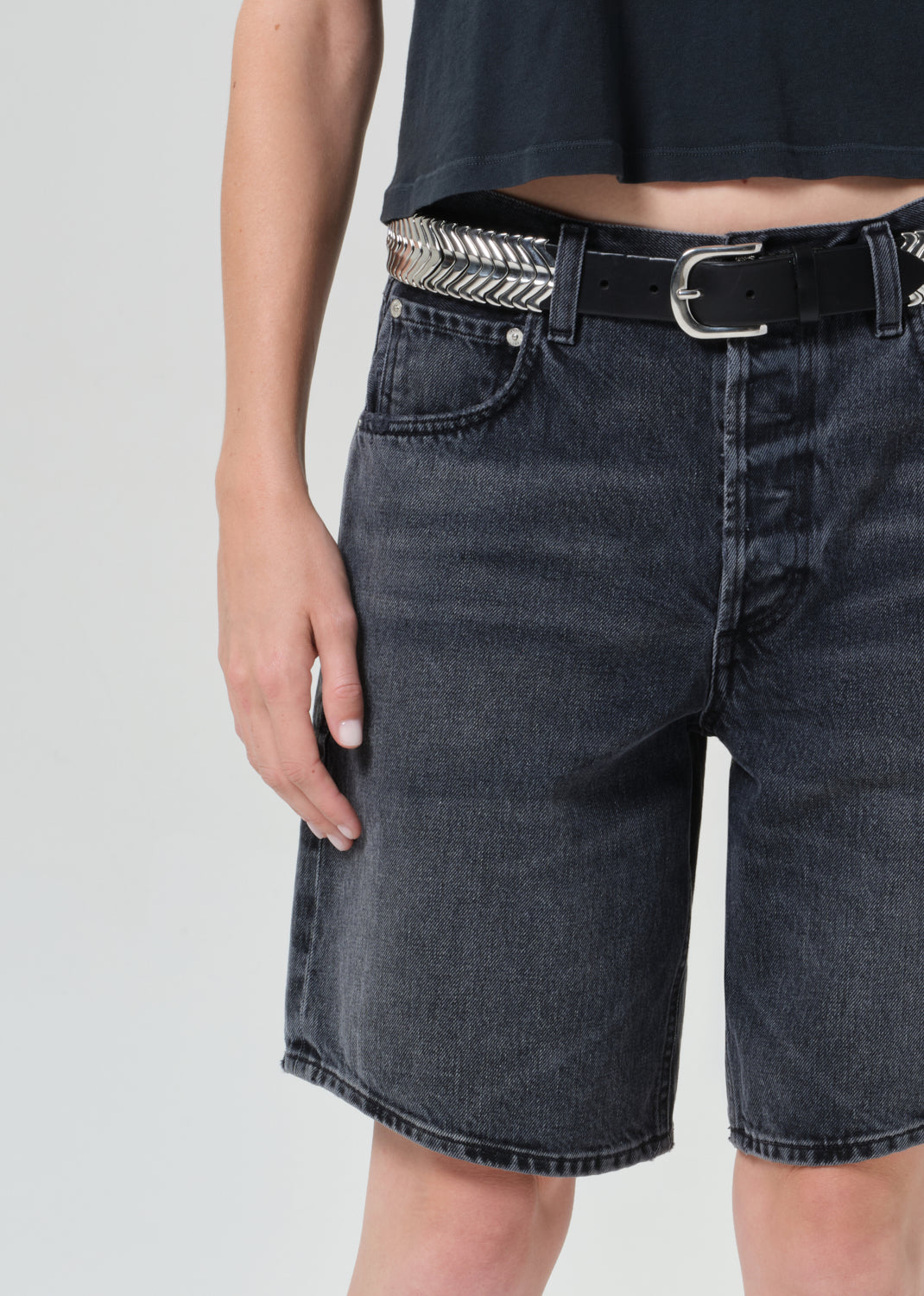 Person wearing black denim shorts and a black crop top on a light gray background