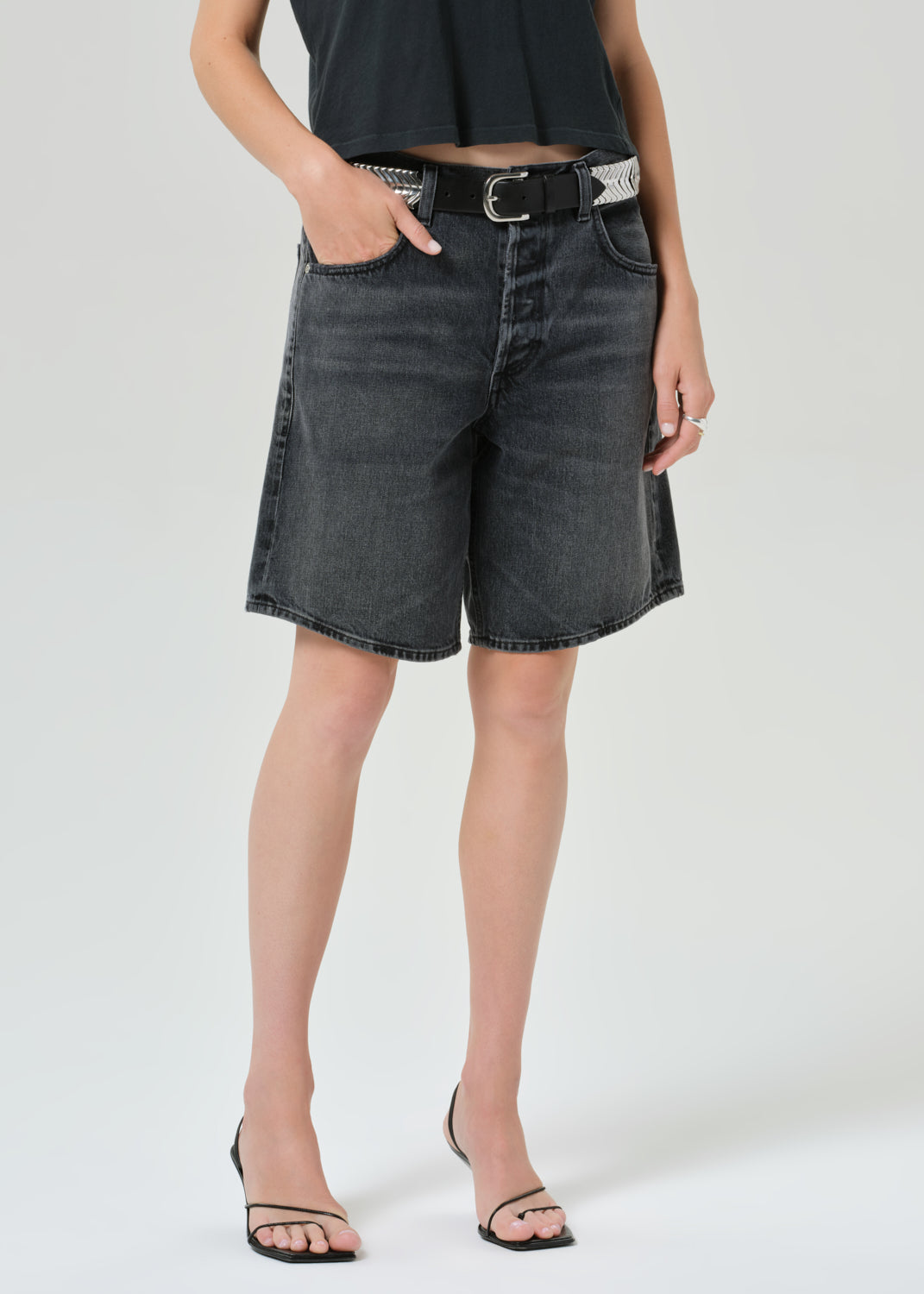 Person wearing black denim shorts on a grey background