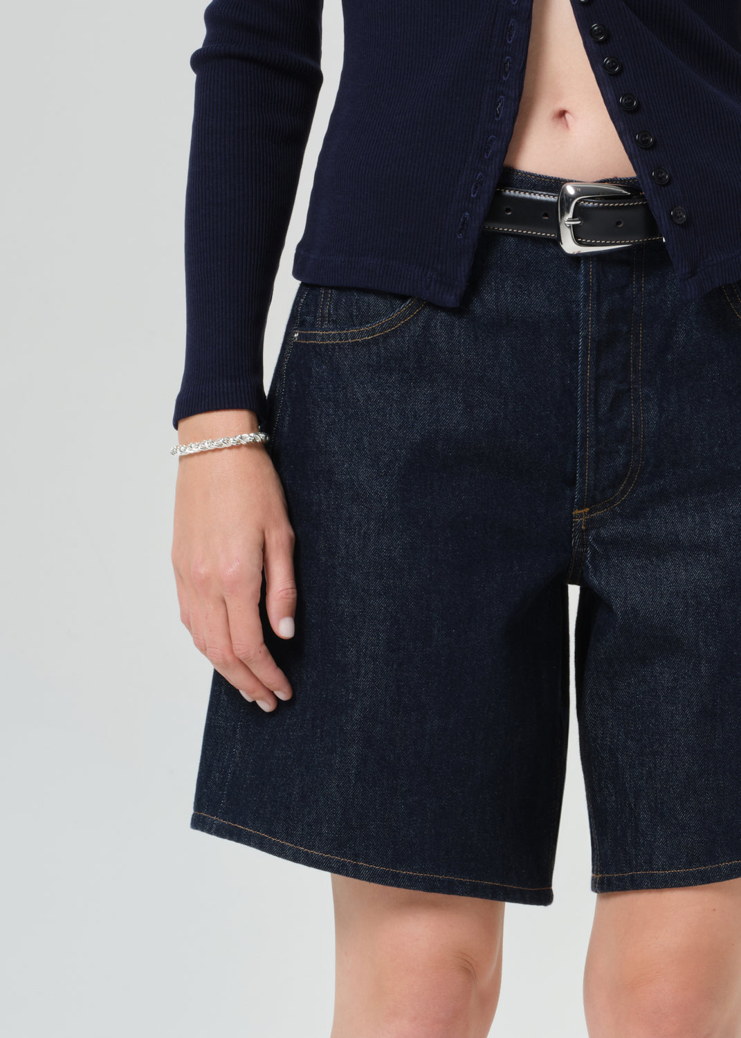 Person wearing a navy cardigan and dark denim shorts on a grey background