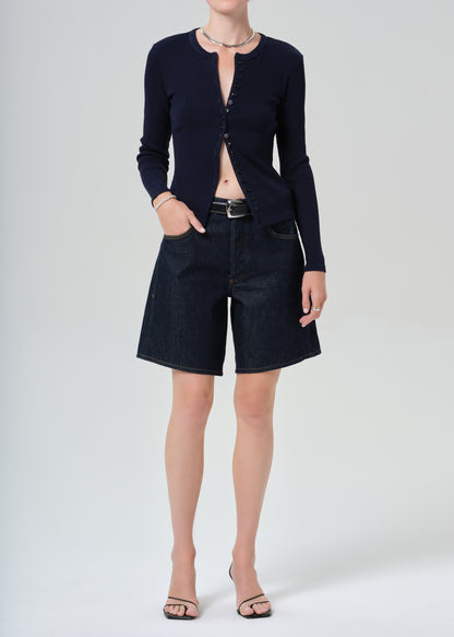 Person wearing a navy cardigan and dark denim shorts on a grey background