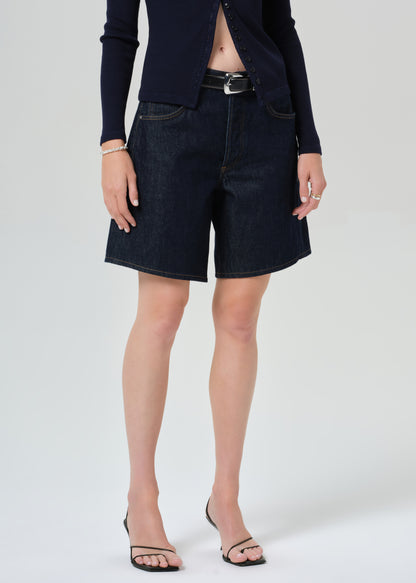 Person wearing a navy cardigan and dark denim shorts on a grey background