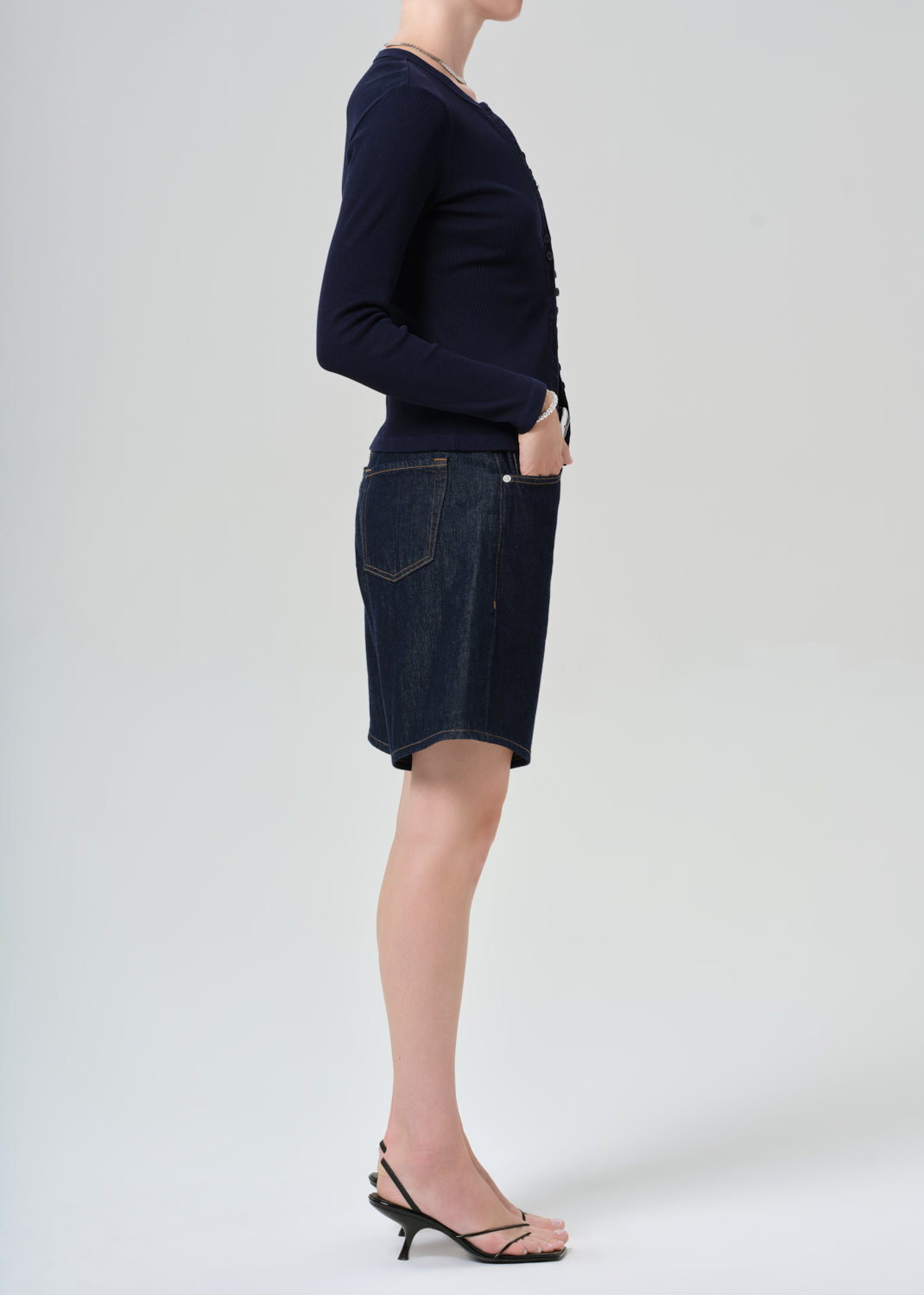 Person wearing a navy cardigan and dark denim shorts on a grey background