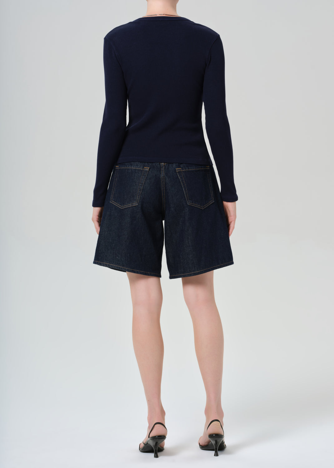 Person wearing a navy cardigan and dark denim shorts on a grey background