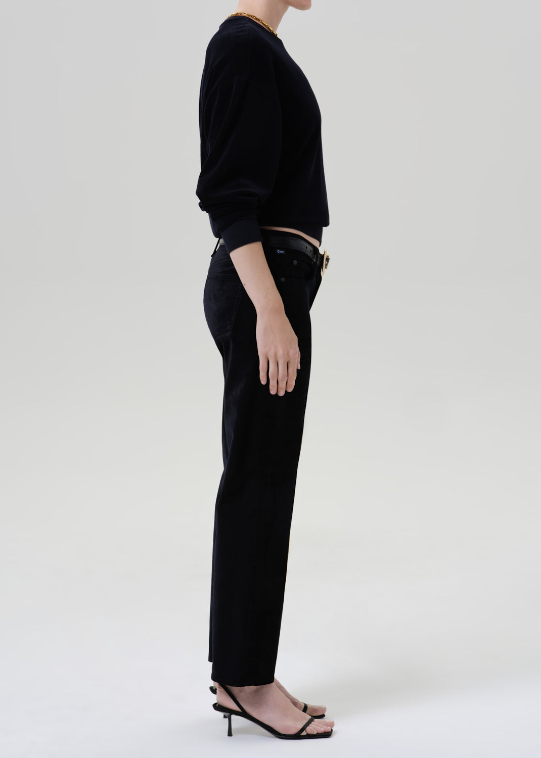 Person wearing black sweater with black pants and belt on a grey background