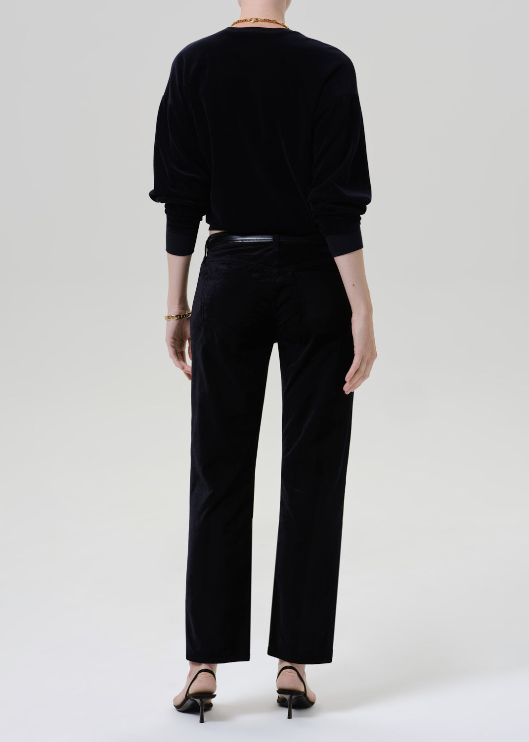 Person wearing black sweater with black pants and belt on a grey background