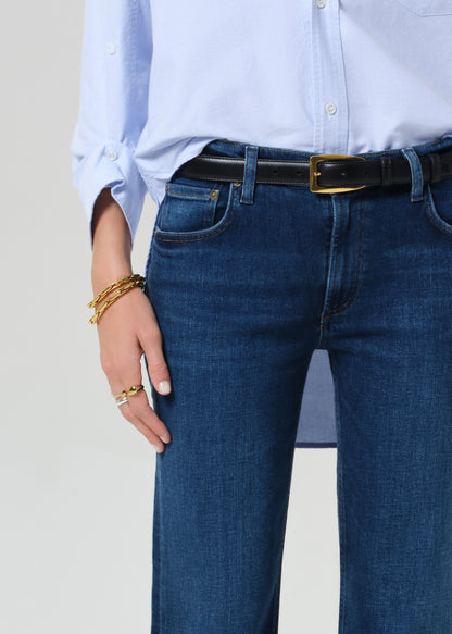 Person wearing a light blue button-up shirt, dark blue jeans, and black boots on a grey background
