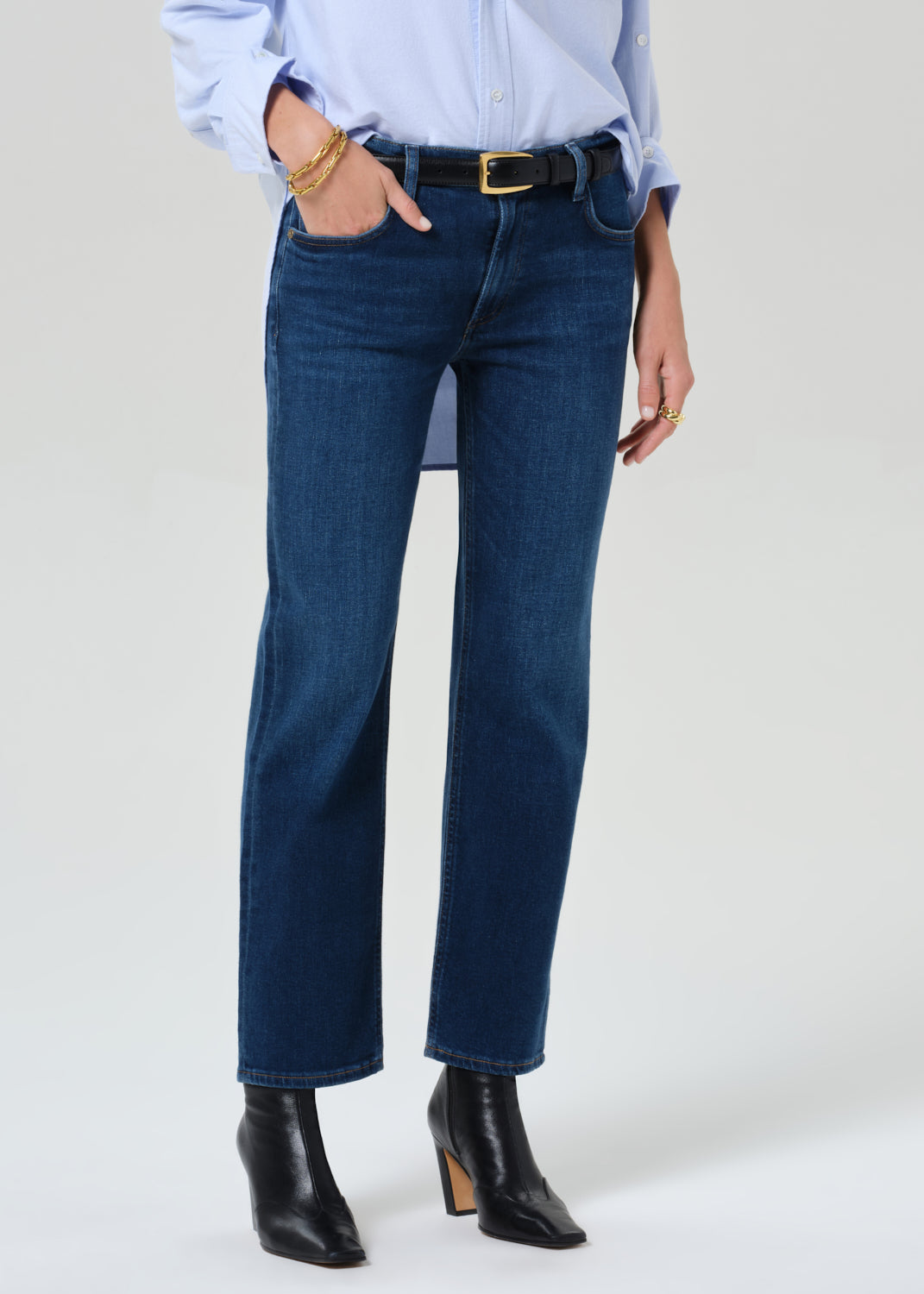 Person wearing a light blue button-up shirt, dark blue jeans, and black boots on a grey background