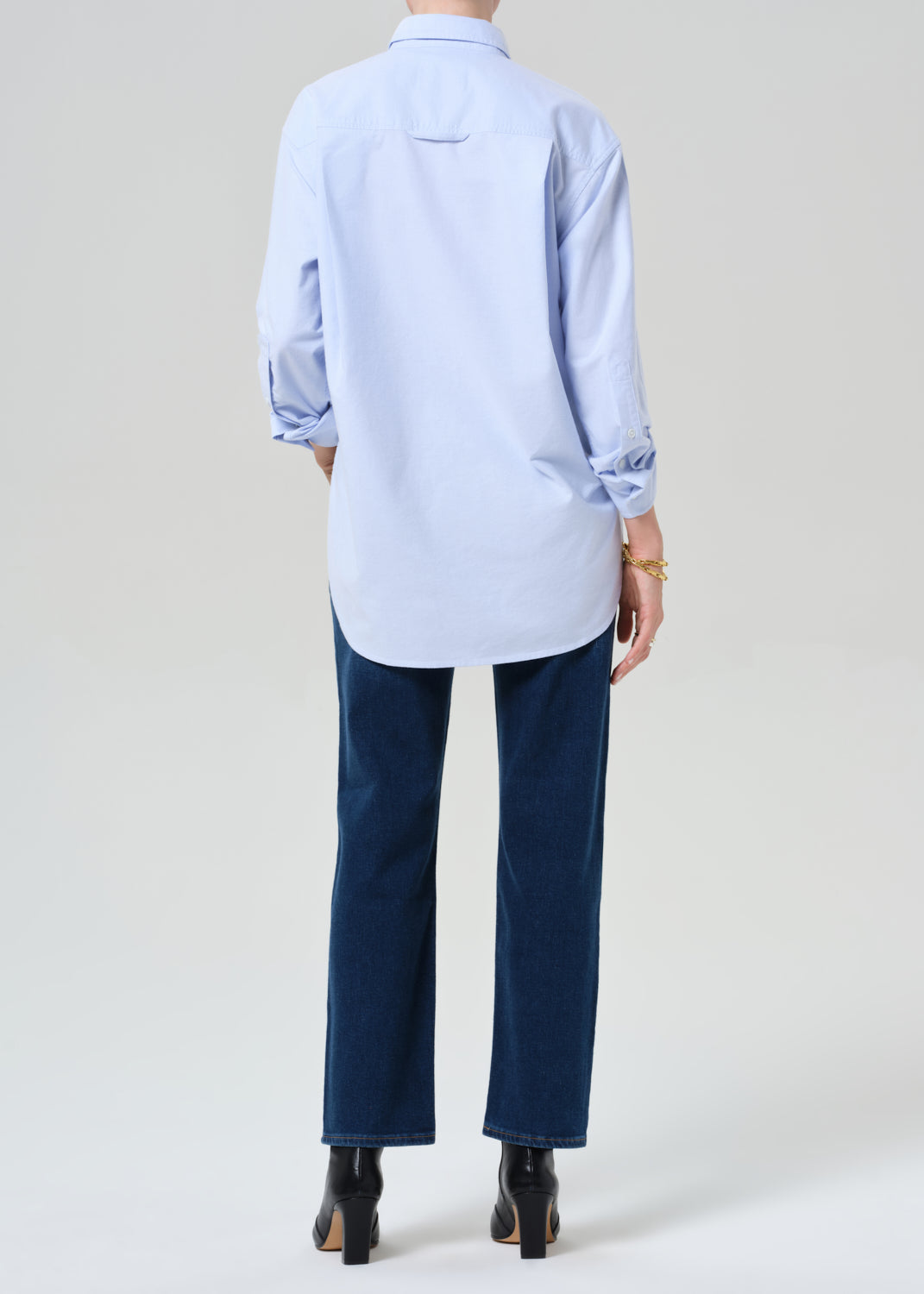 Person wearing a light blue button-up shirt, dark blue jeans, and black boots on a grey background