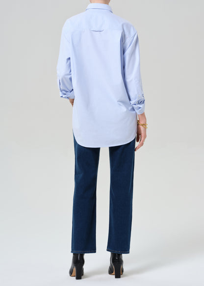 Person wearing a light blue button-up shirt, dark blue jeans, and black boots on a grey background