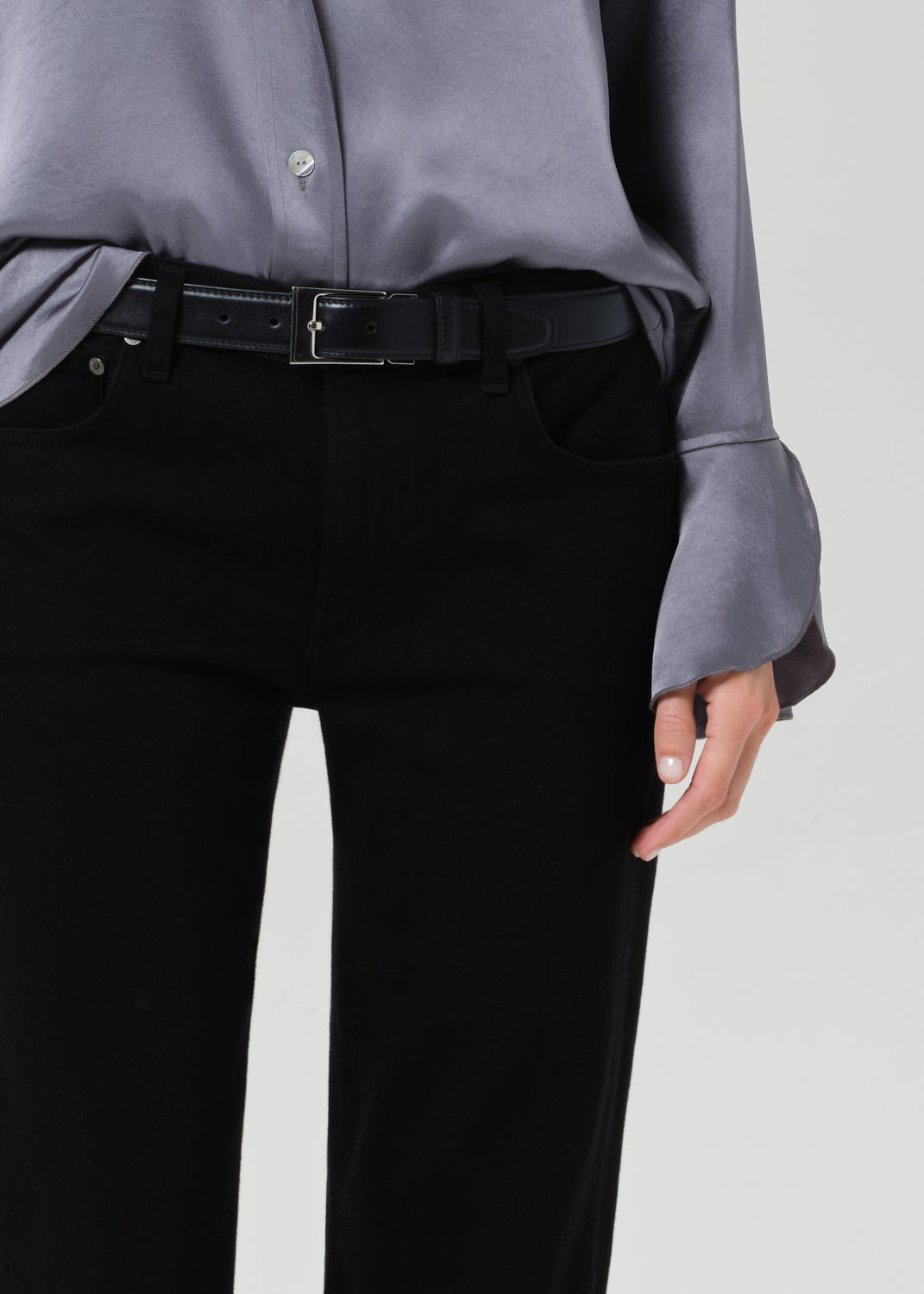 Person wearing a gray button-up shirt and black jeans on a grey background