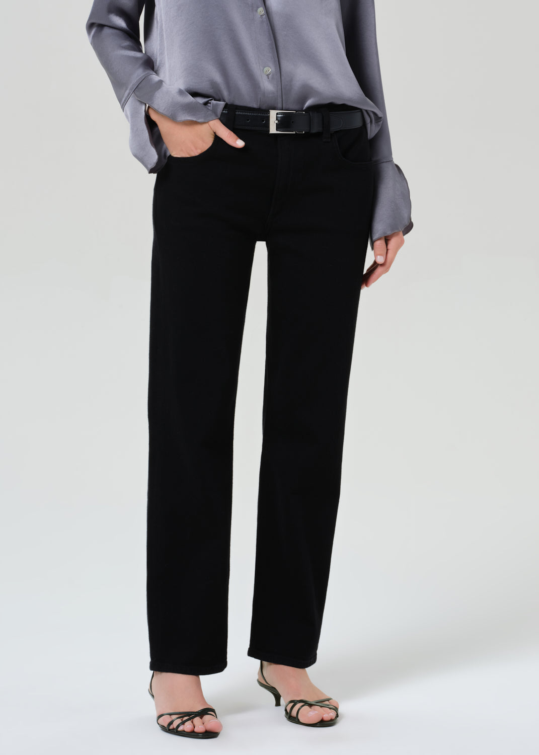 Person wearing a gray button-up shirt and black jeans on a grey background