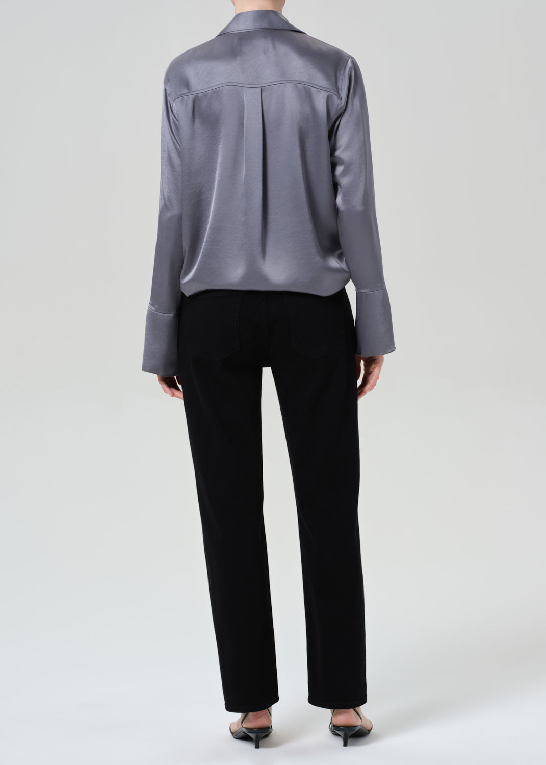 Person wearing a gray button-up shirt and black jeans on a grey background