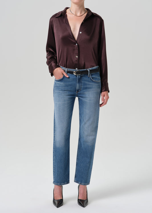 A model wearing a dark brown satin button-down shirt, blue jeans with a black belt, and black heels, photographed against a grey background.