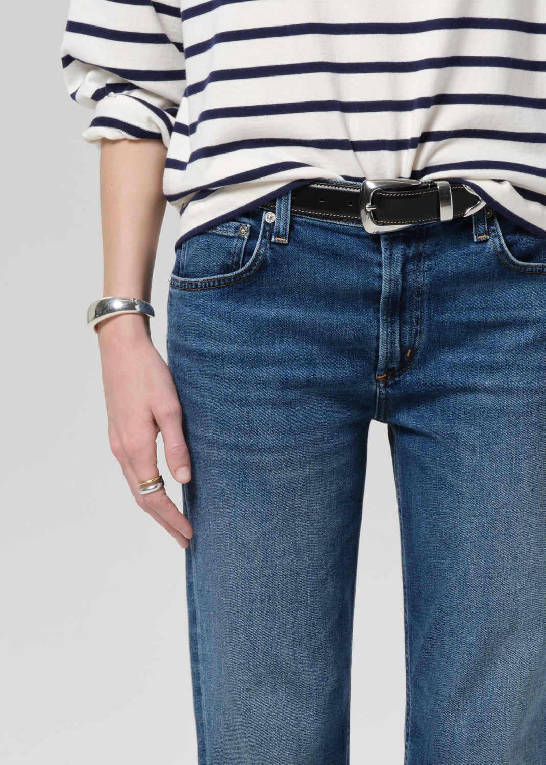 Person wearing a striped shirt and blue jeans on a grey background