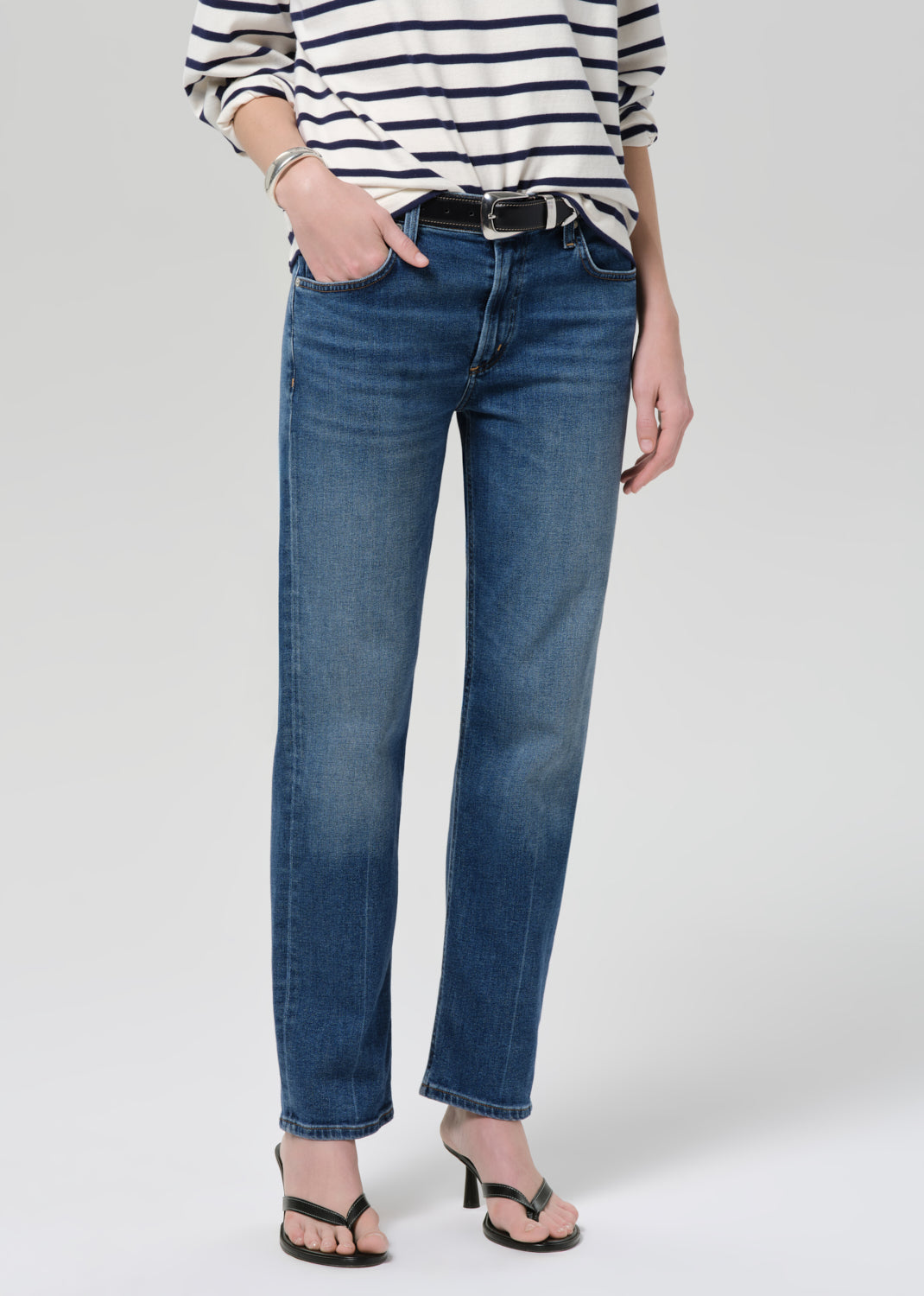 Person wearing a striped shirt and blue jeans on a grey background