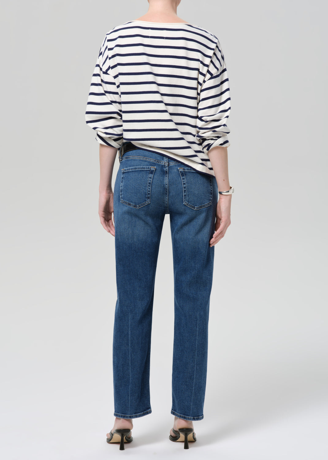 Person wearing a striped shirt and blue jeans on a grey background