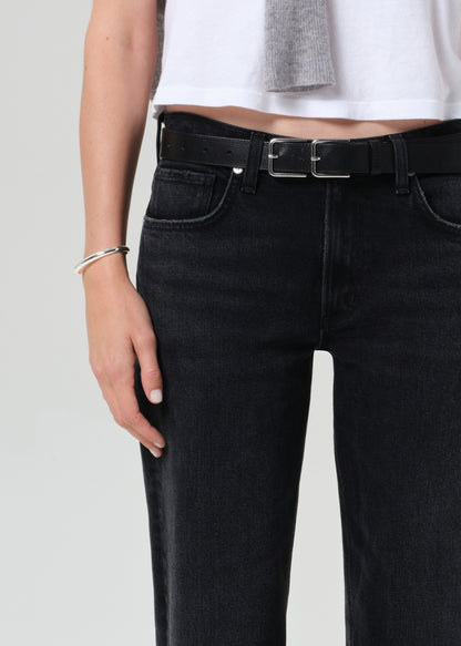 Person wearing a white top, black jeans, and a gray sweater on a plain background