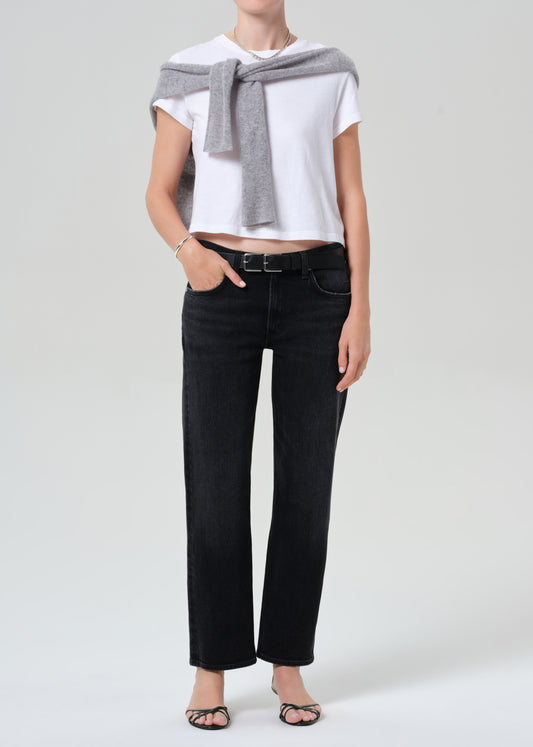 Person wearing a white top, black jeans, and a gray sweater on a plain background