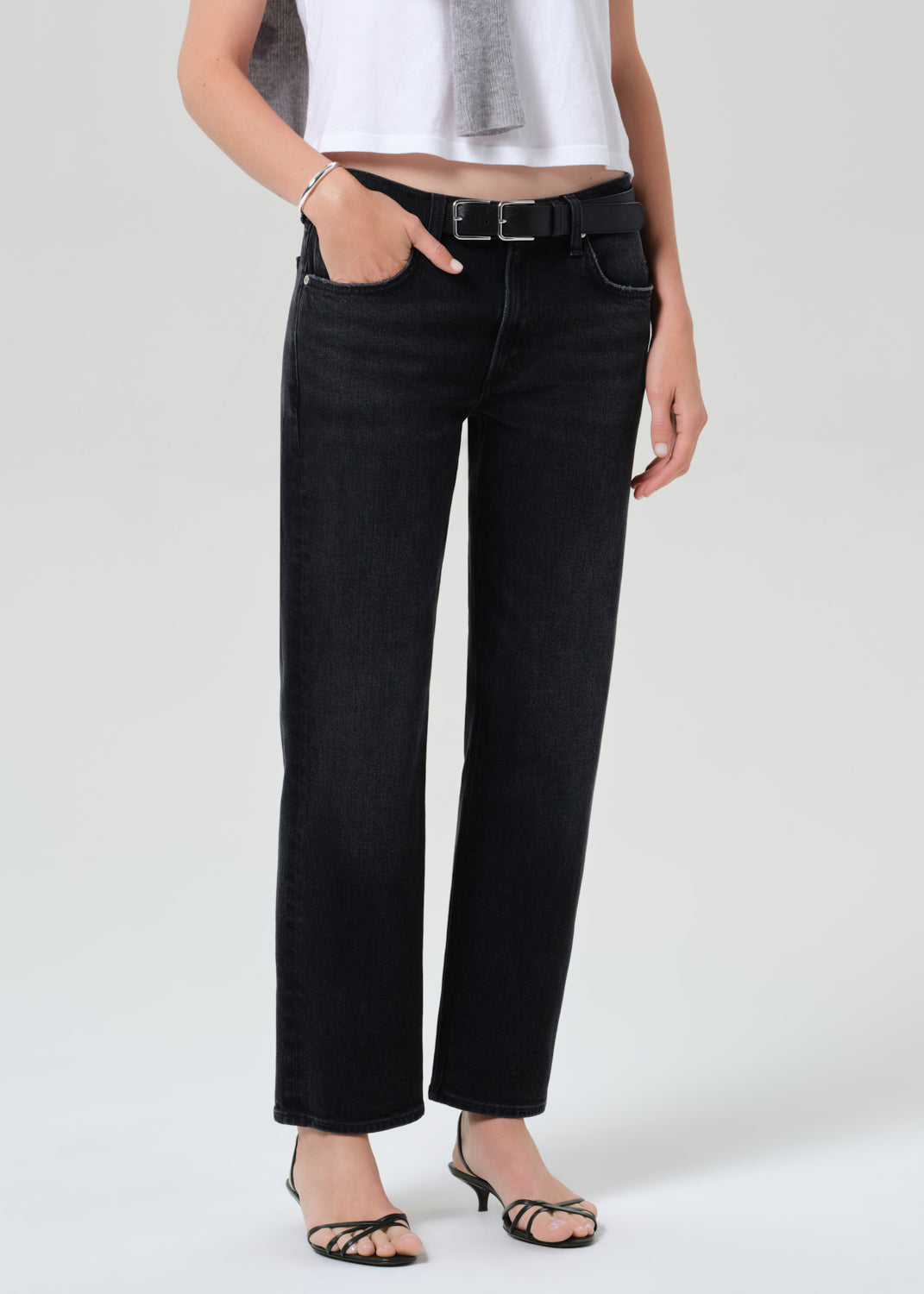 Person wearing a white top, black jeans, and a gray sweater on a plain background