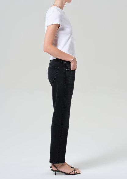 Person wearing a white top, black jeans, and a gray sweater on a plain background