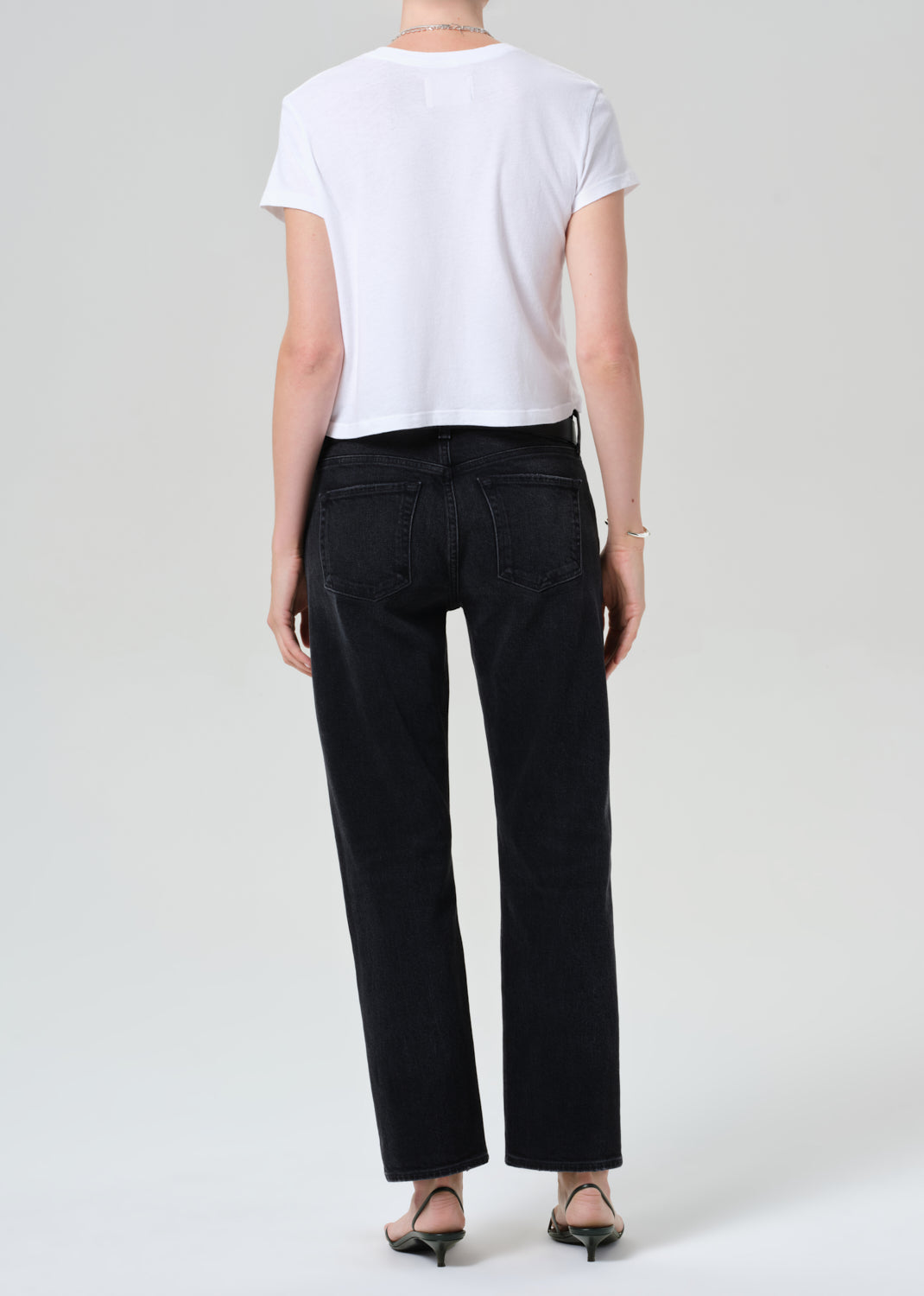 Person wearing a white top, black jeans, and a gray sweater on a plain background