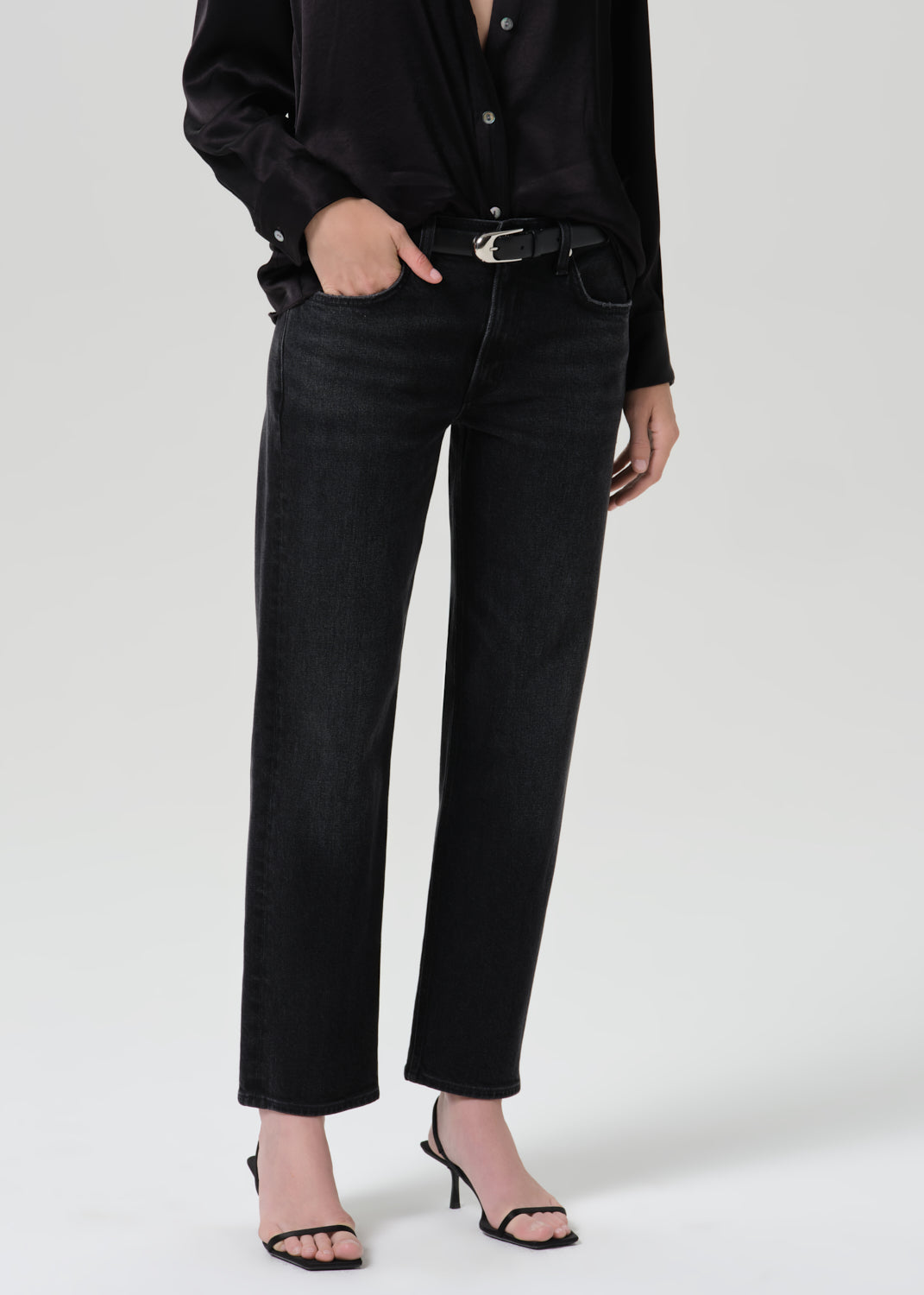 A model wearing black wide-leg cropped jeans with a black shirt and black heeled sandals, shown from the chest down against a grey background.