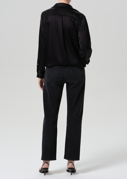 A model shown from the back wearing a black satin long-sleeve shirt and black wide-leg jeans, paired with black pointed-toe heels, against a grey background.