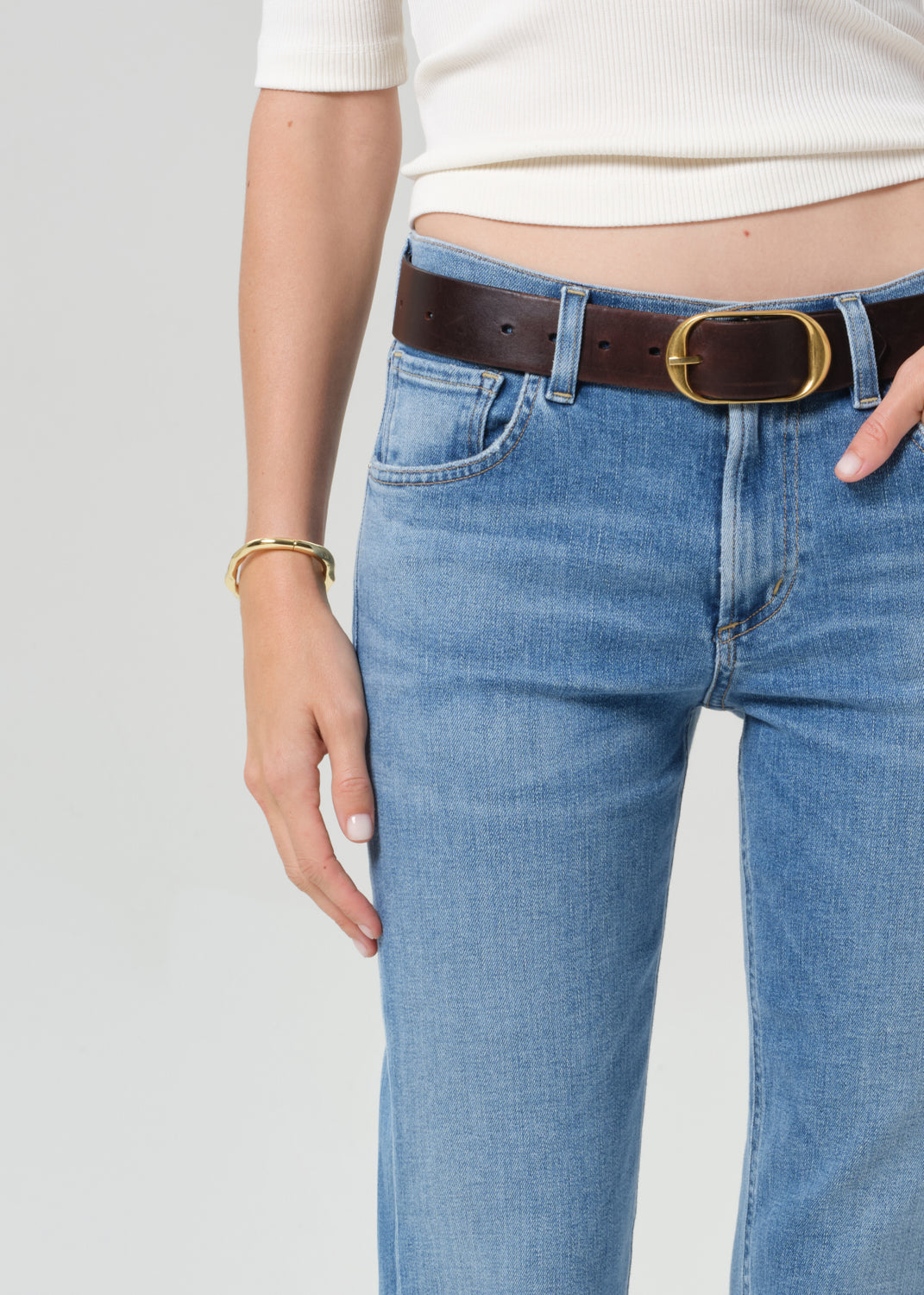 Person wearing blue jeans with a brown belt on a plain background