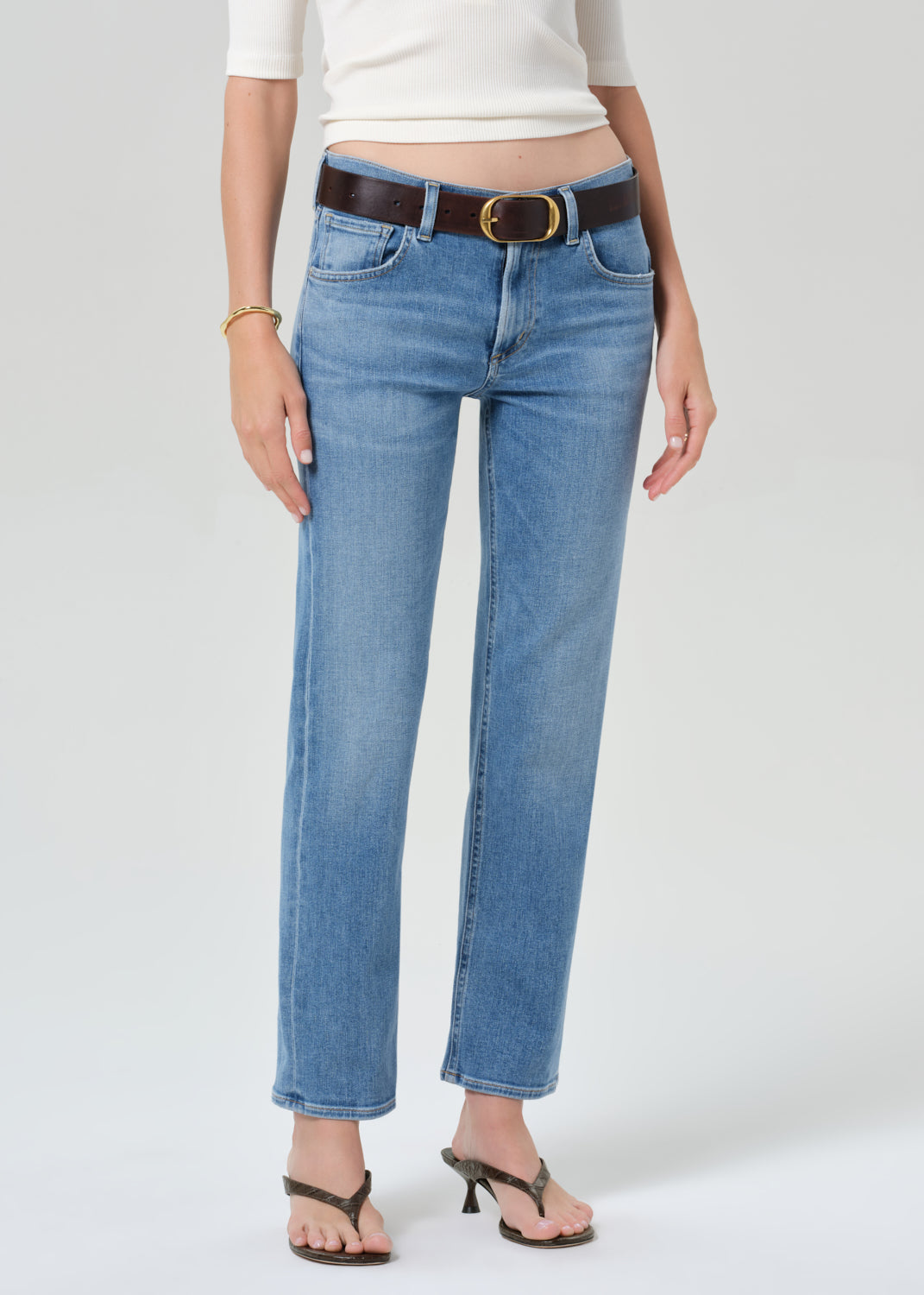 Person wearing blue jeans with a brown belt on a white background