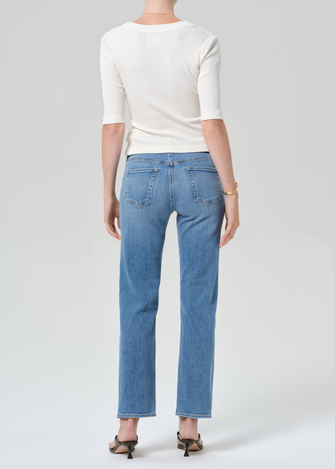 Person wearing a white top and blue jeans on a plain background