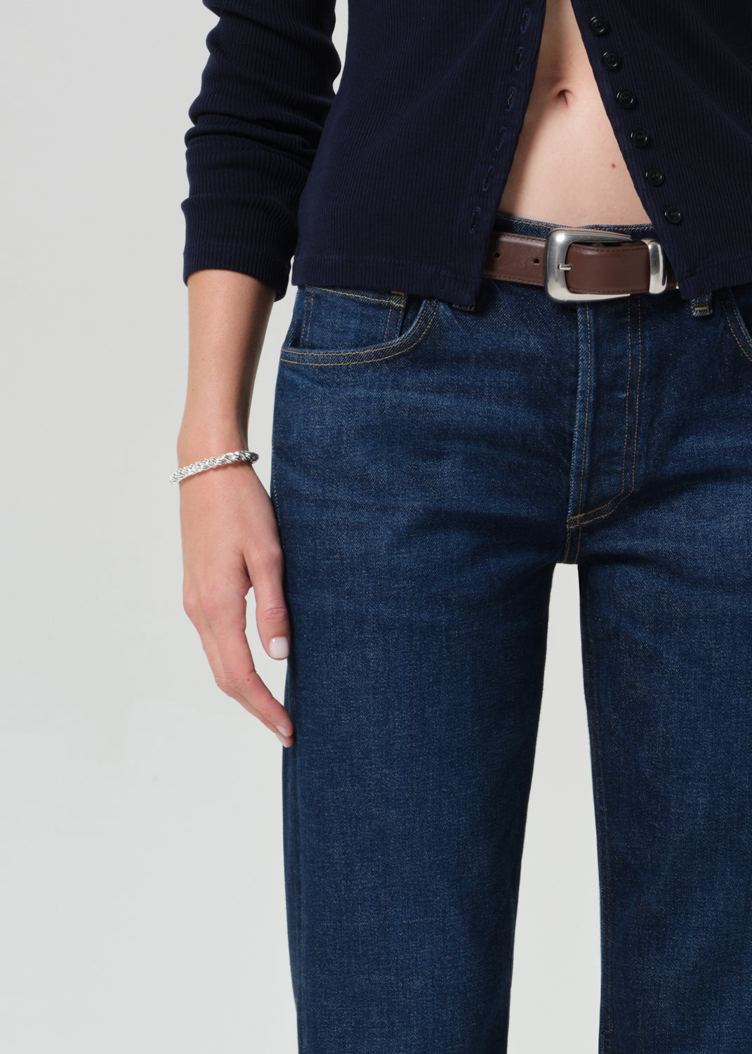 Person wearing a navy cardigan and dark blue jeans on a grey background