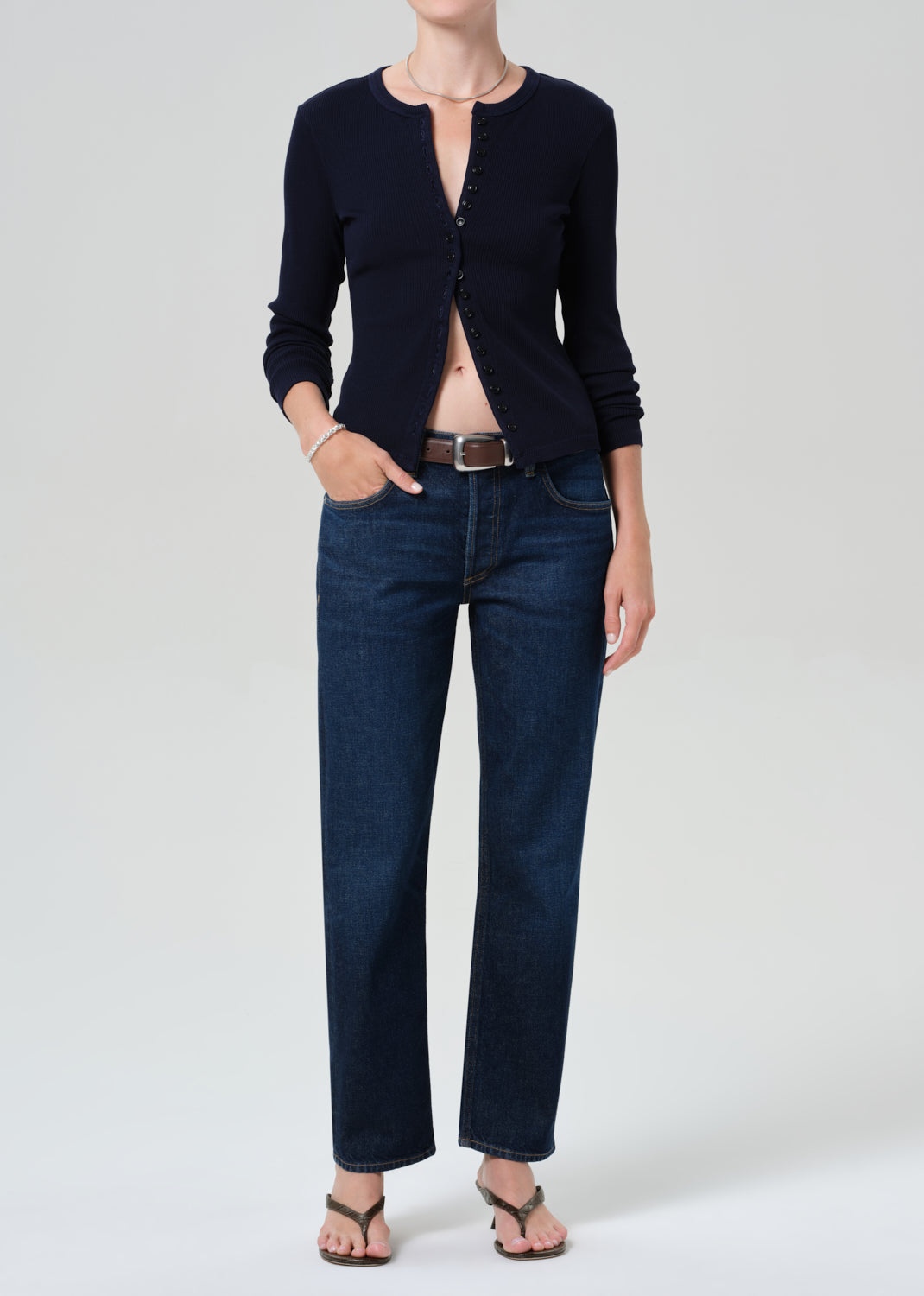 Person wearing a navy cardigan and dark blue jeans on a grey background